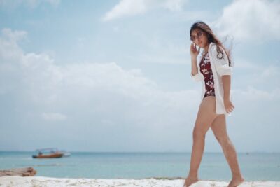 photo of woman in floral swimsuit and white dress shirt standing on her toes at a beach