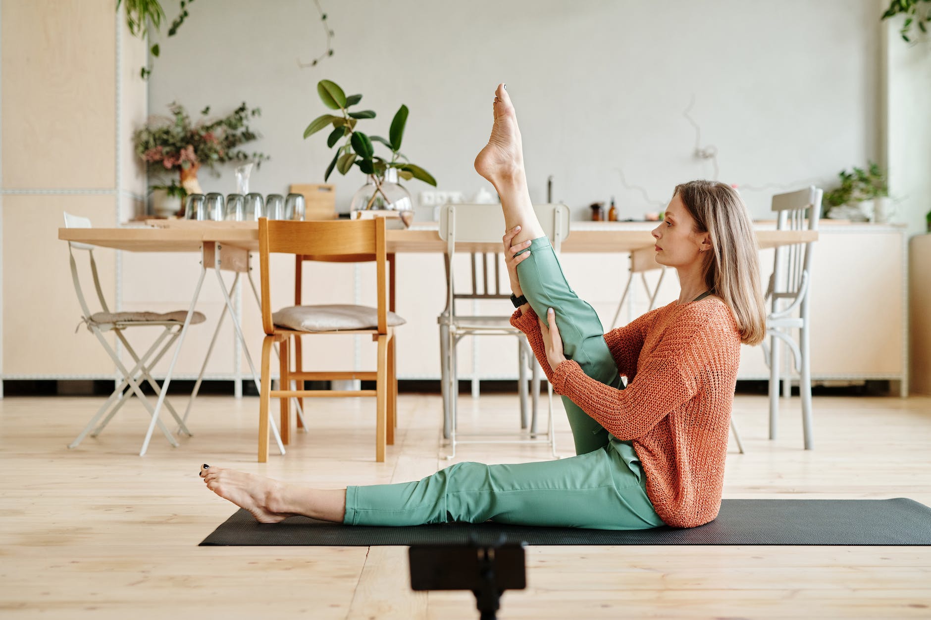 woman in brown sweater and green pants sitting on black yoga mat