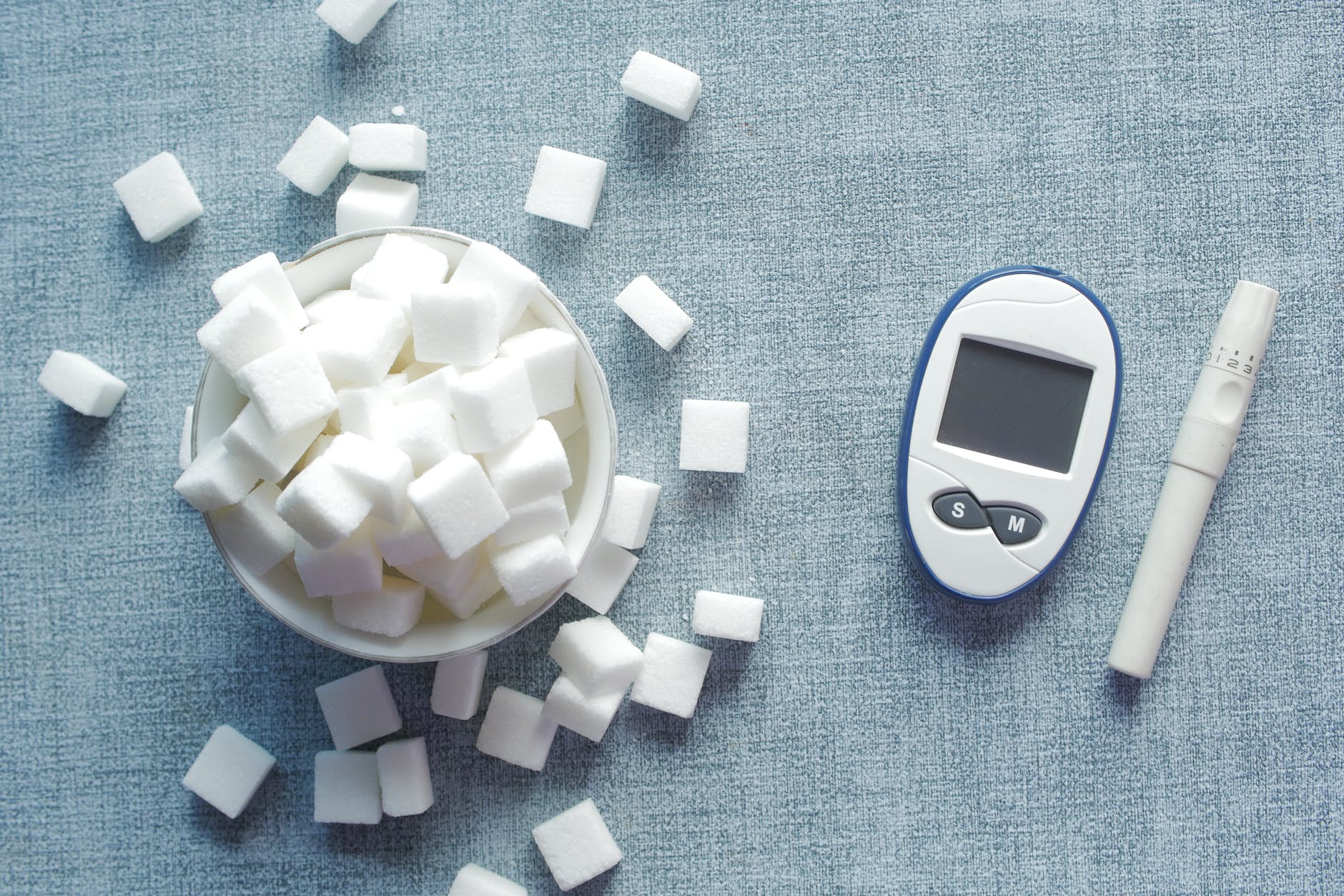bowl of sugar cubes beside a glucometer and a syringe pen
