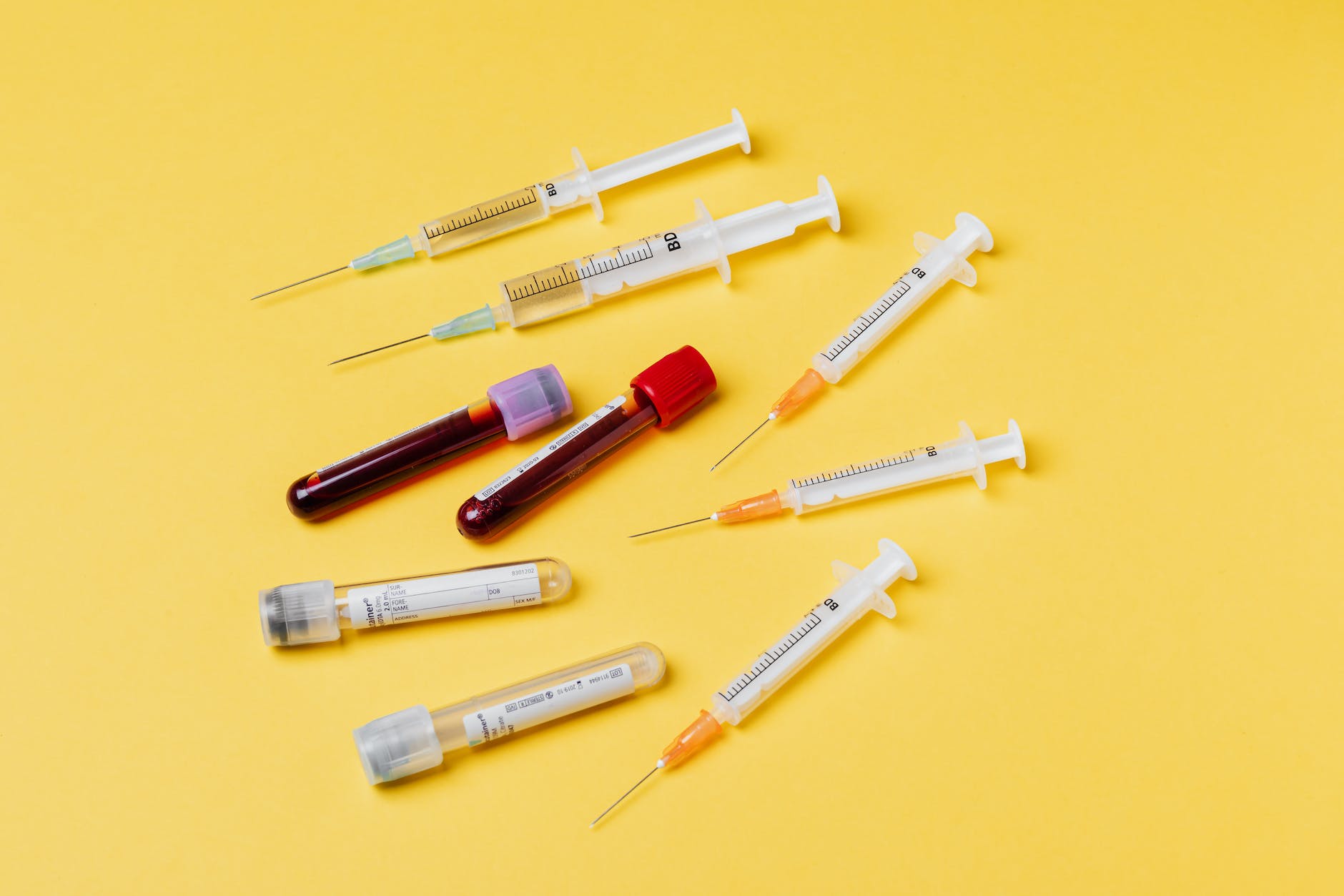 clinical blood collection tubes and syringes on yellow background