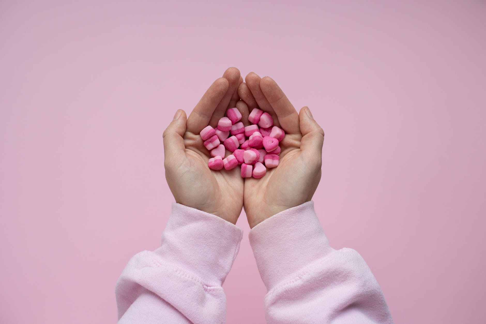 person holding pink candies in form in hearts in hands
