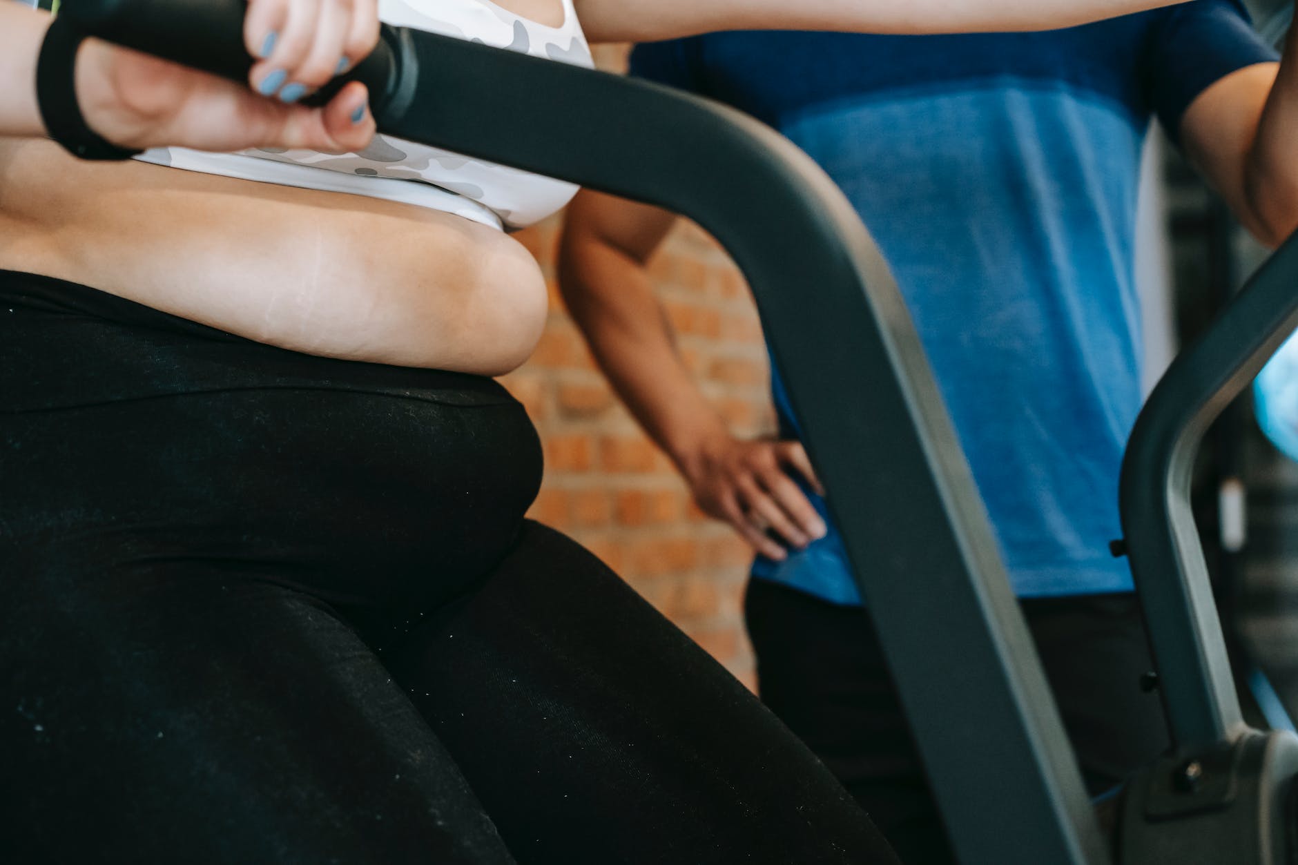 a personal trainer standing by a woman exercising on cycling machine