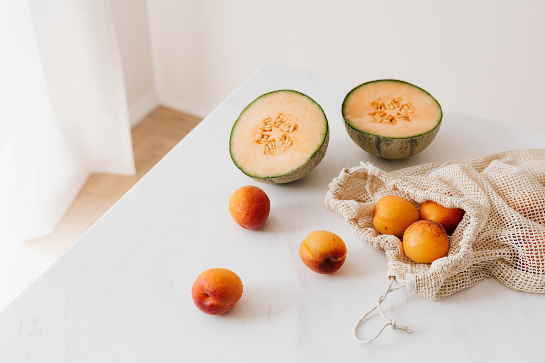 jute sack with ripe apricots on table near halved appetizing melon